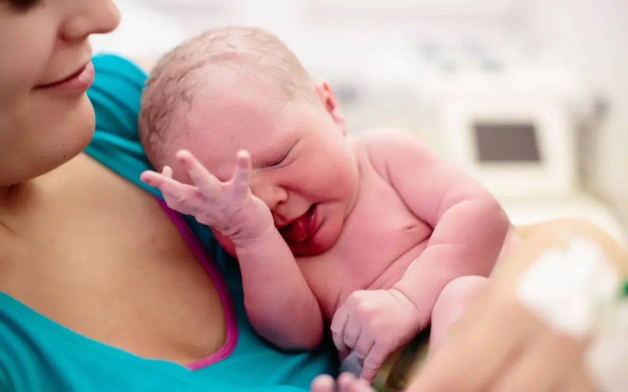 Neugeborenes Baby wird von der Mutter gehalten. Die Nabelschnur wird auspulsieren gelassen, um dem Kind alle wichtigen Nährstoffe zu übergeben.