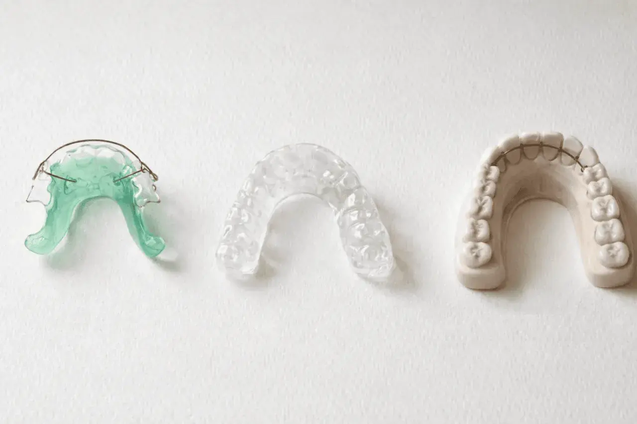 Tres dispositivos dentales: un retenedor verde, un retenedor transparente y un modelo de dientes con barra retenedora.