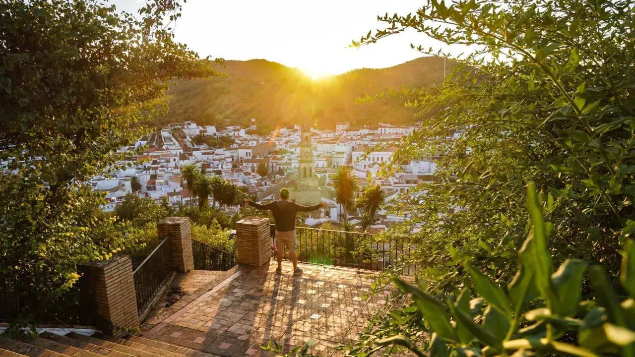 Hombre con brazos abiertos contempla un pueblo blanco en la sierra de Sevilla al atardecer.