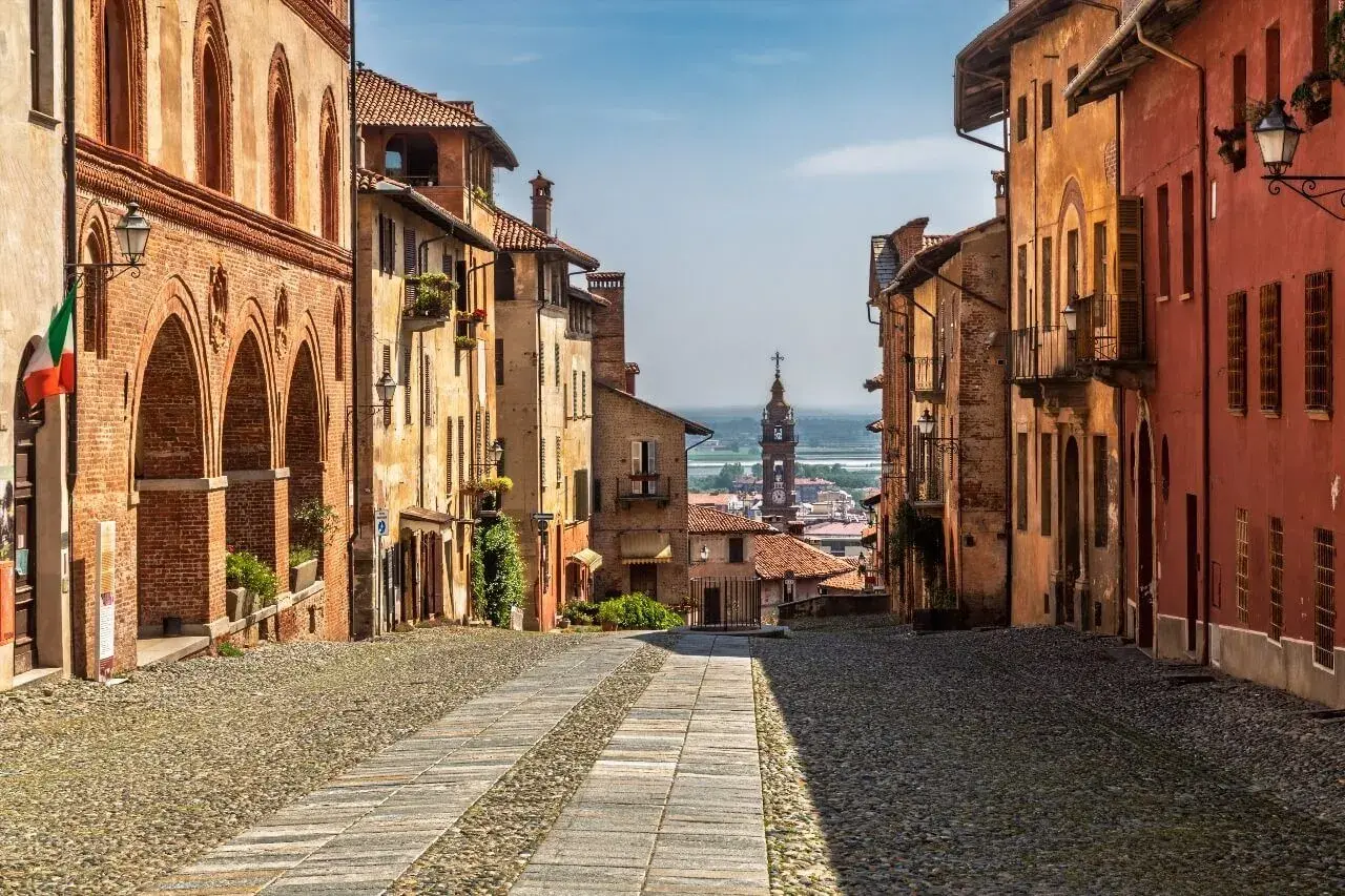 Rue pavée bordée de maisons colorées, avec une église au loin. Un charmant village du Piémont, Italie.