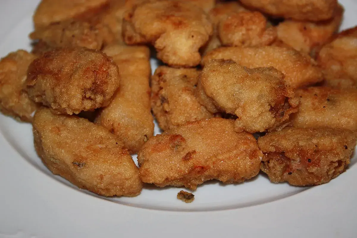 Un plato blanco lleno de trozos dorados y crujientes de japuta en adobo, listos para disfrutar.