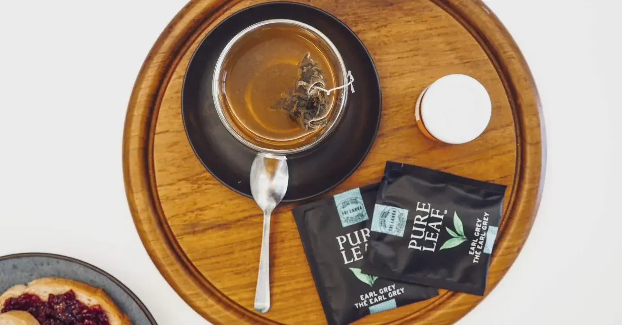 Aromatyczna, najlepsza czarna herbata Earl Grey z Sri Lanki, zaparzona w szklance, obok saszetki i łyżeczka.