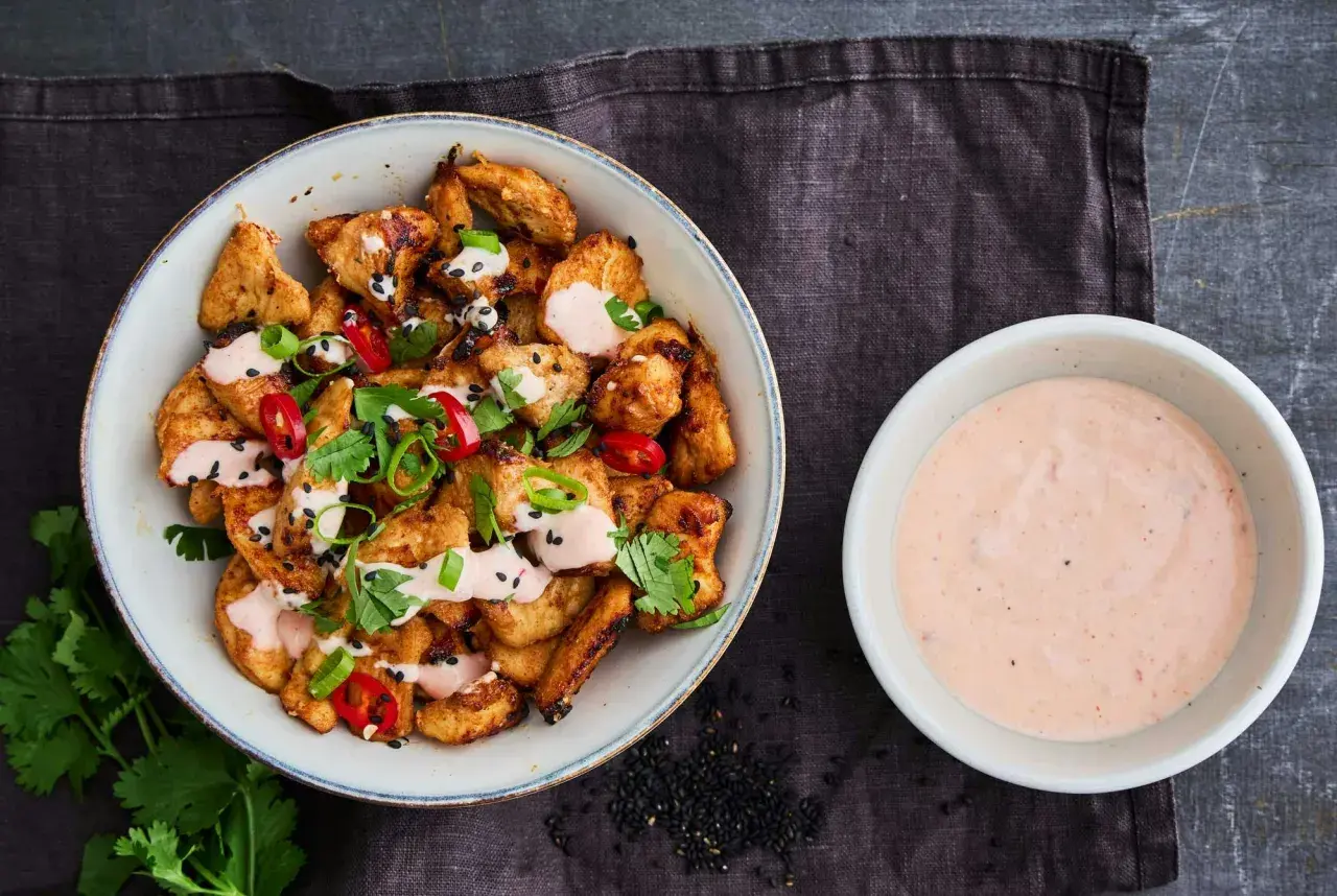 Krispiga kycklingbitar toppade med färska örter, chili och sesamfrön, serverade med en krämig bang bang sås.