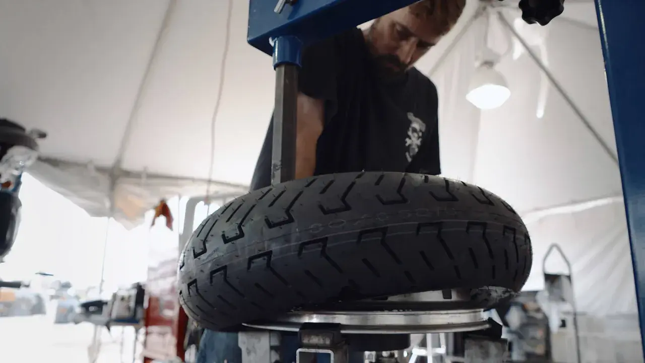 Mecánico revisa un neumático de moto con inscripción 100/90 r18 equivalencia.