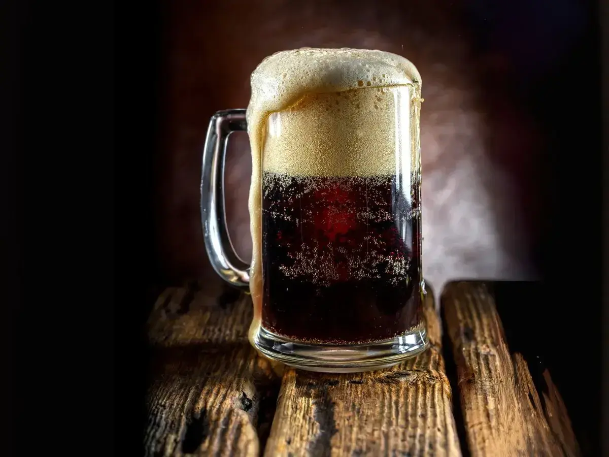 Boccale di birra scura con schiuma abbondante, forse la birra americana più famosa, su un tavolo di legno rustico.