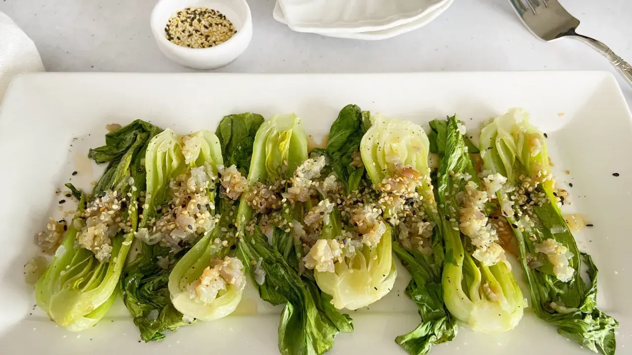 Bok choy tierno salteado con ajo y semillas de sésamo, servido en un plato blanco.