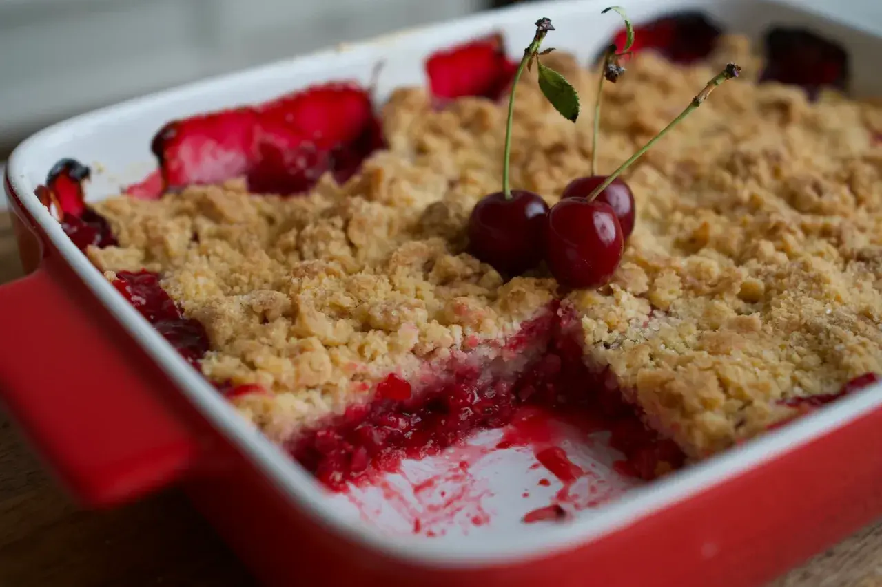 Un délicieux crumble fruits rouges, garni de cerises fraîches, sort du four.