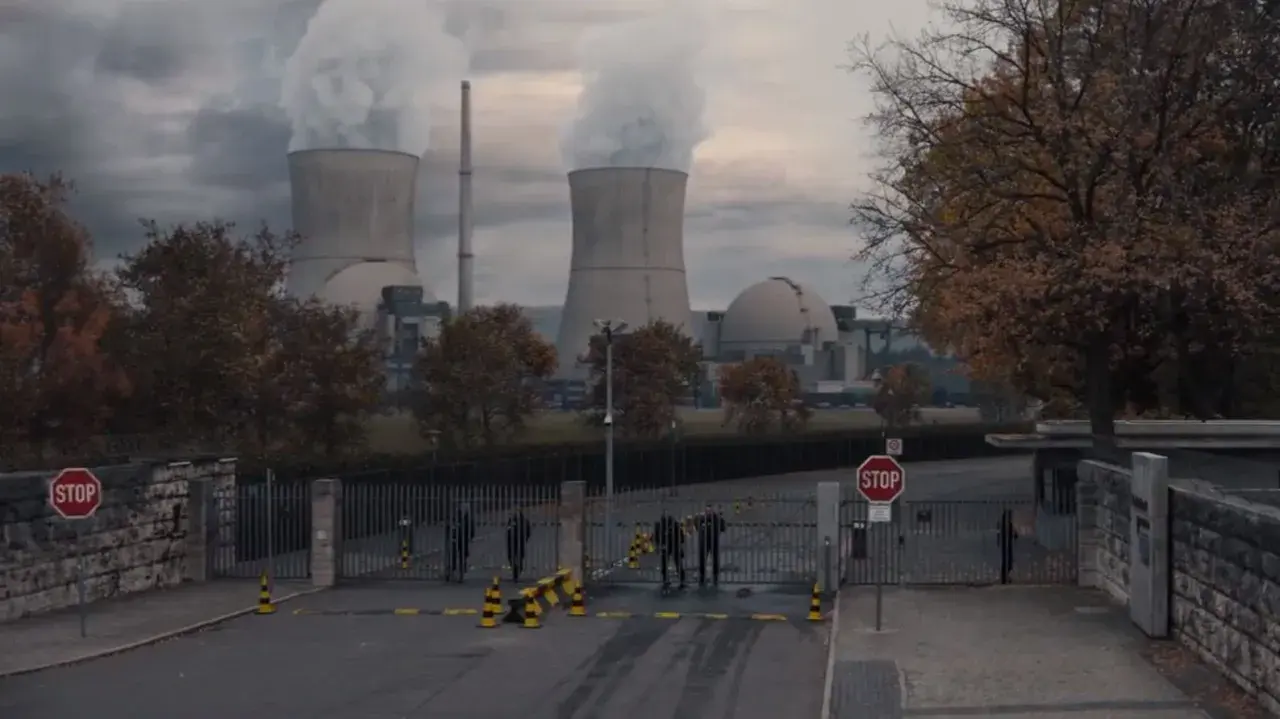 Mroczna elektrownia z chmurami pary nad chłodniami. Strażnicy przy bramie, nie wiadomo, kto jest kim.