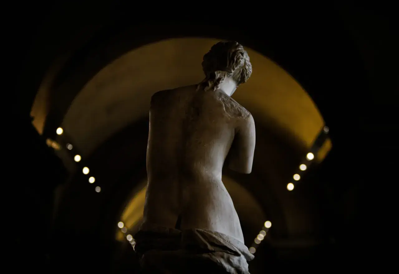 Statue de la déesse de l'amour, vue de dos, dans une lumière tamisée.