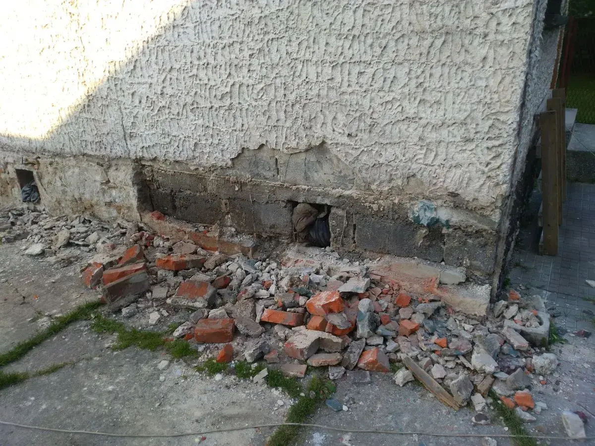 Odkopany fragment ściany z widocznymi uszkodzeniami, gruz i cegły. Rozpoczęcie prac, jak wzmocnić stare fundamenty z kamienia.