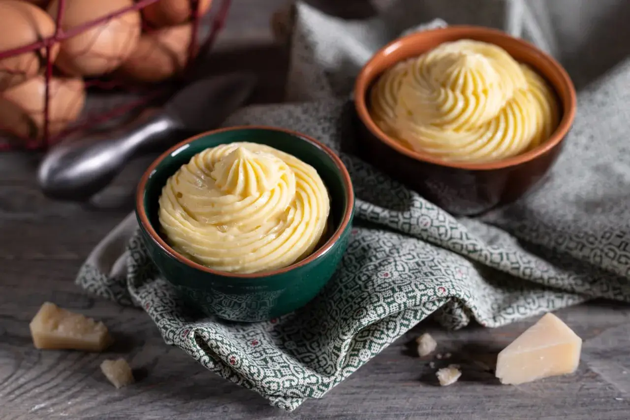 Due ciotole con crema pasticcera salata, guarnita a spirale. In sottofondo uova e formaggio.