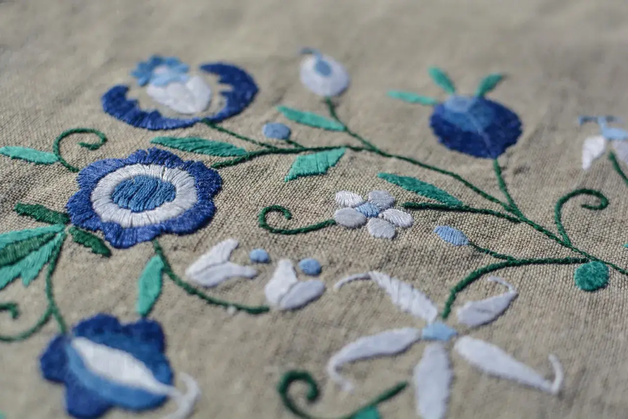 Un fichier broderie aux motifs floraux bleus et blancs sur fond beige. Les détails des points de couture sont visibles.
