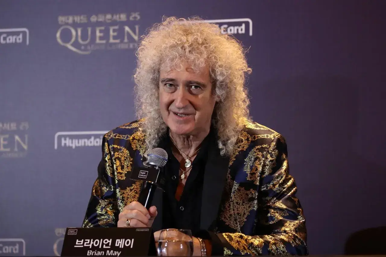 Brian May z zespołu Queen, w ozdobnej marynarce, udziela wywiadu.