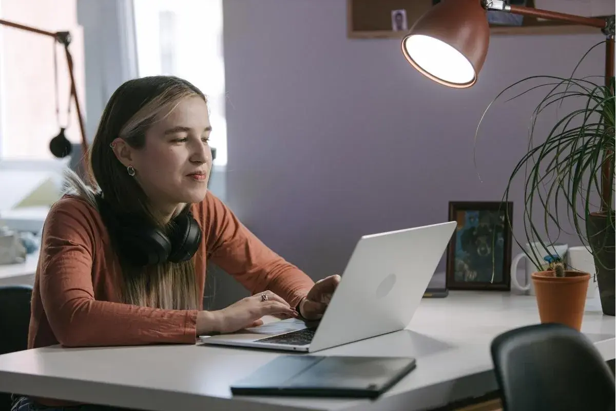 Młoda kobieta z słuchawkami na szyi pracuje na laptopie, być może instaluje aplikację z nieznanych źródeł, ryzykując bezpieczeństwo danych.