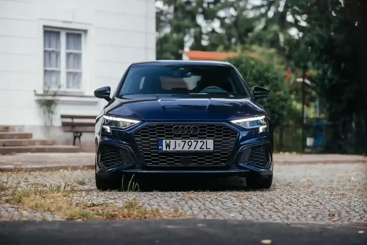 Granatowy Audi A3, segment c, z charakterystycznym grillem i ostrymi światłami, zaparkowany na brukowanej drodze.