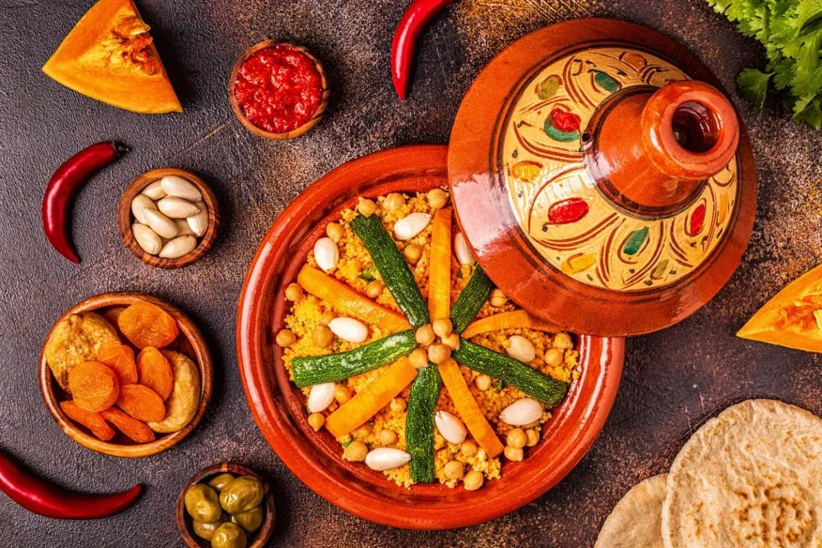 Un colorato cous cous marocco, con verdure, mandorle e albicocche secche, servito in una tajine decorata.