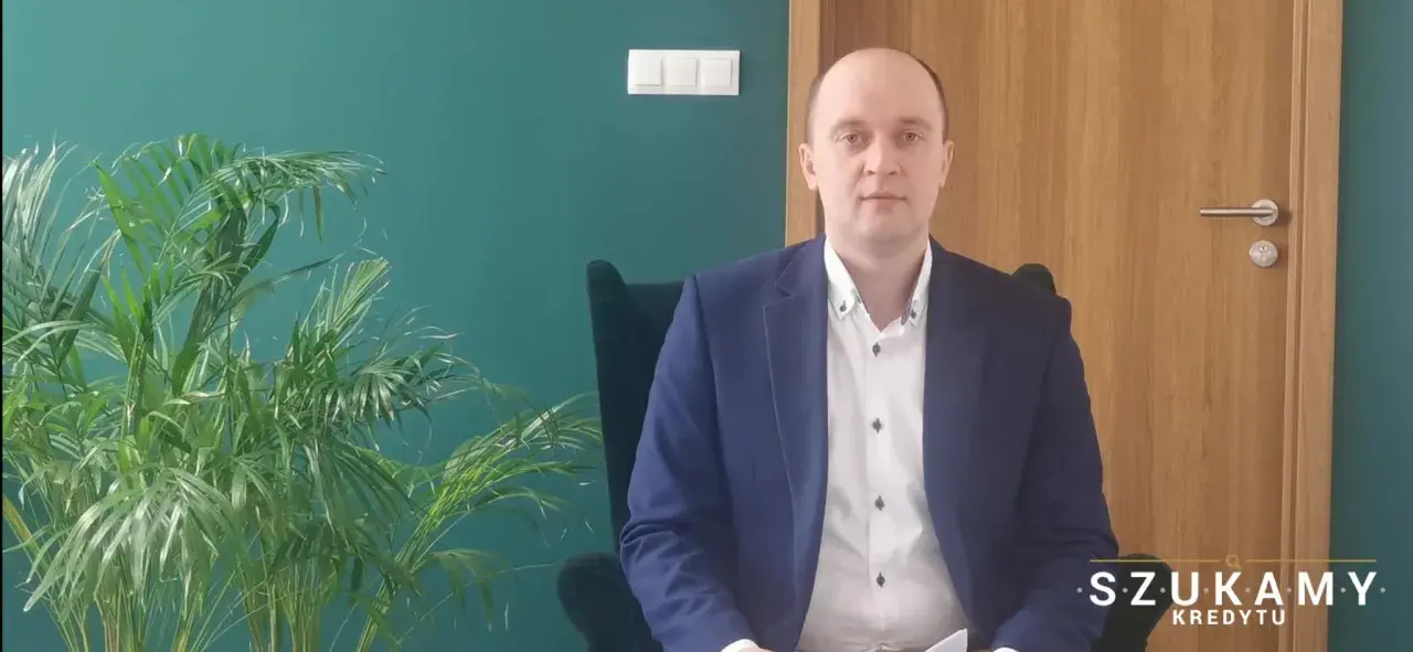 Mężczyzna w garniturze siedzi w fotelu obok rośliny.