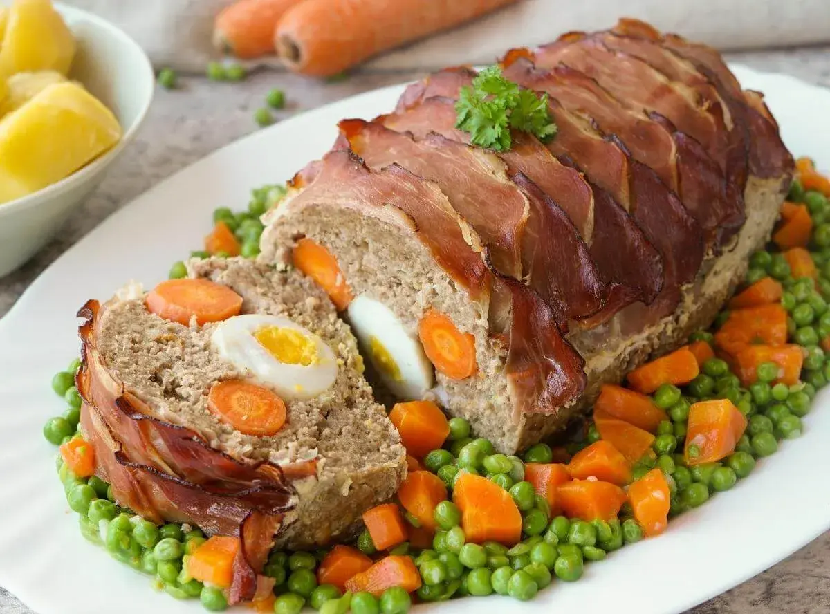 Ein saftiger falscher Hase, umwickelt mit Speck, serviert auf Erbsen und Karotten.