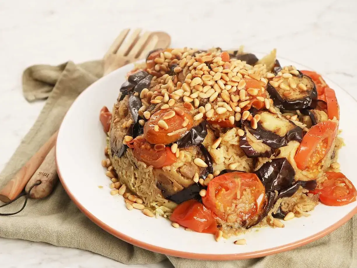 En läcker maklobe kyckling med aubergine, tomater och pinjenötter, serverad på en vit tallrik.
