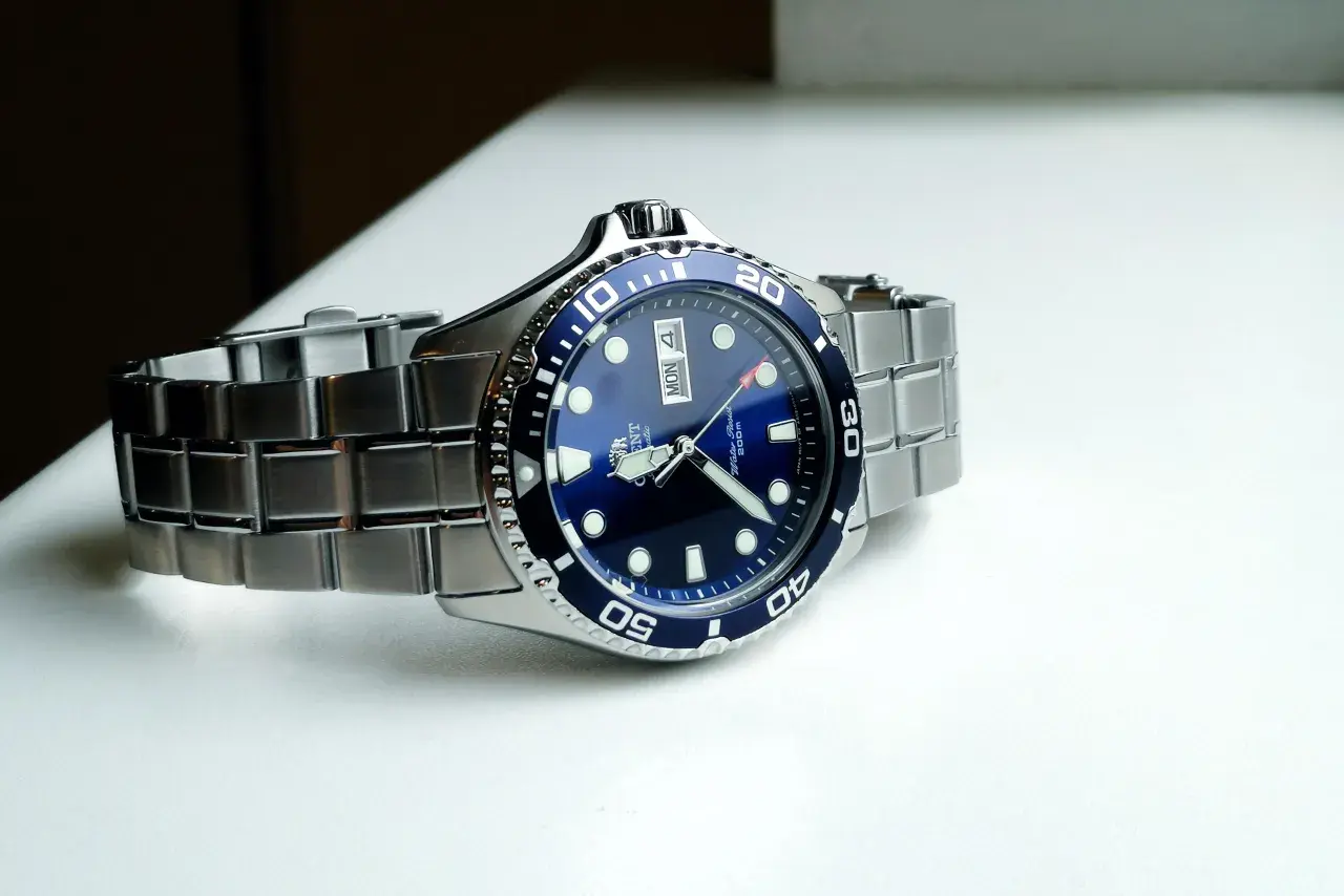 En blå dykarklocka, Orient Ray II, med ett silverfärgat armband ligger på en vit yta.