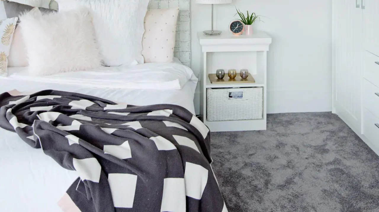 Un letto accogliente con coperta a quadri e un morbido tappeto grigio, perfetto per la posa moquette.