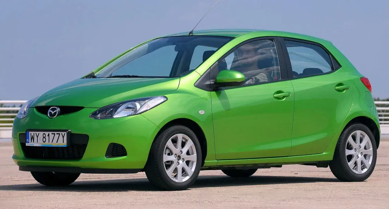Zielona Mazda 2 DE z polskimi tablicami rejestracyjnymi WY 8177Y stoi na zewnątrz.