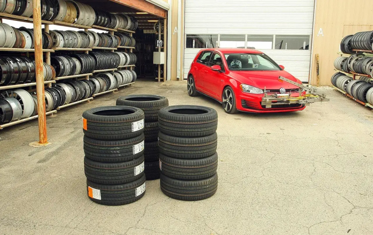 Test opon letnich 225/45 r17. Czerwony VW Golf GTI z zamontowanym sprzętem do pomiarów stoi obok stosów nowych opon.