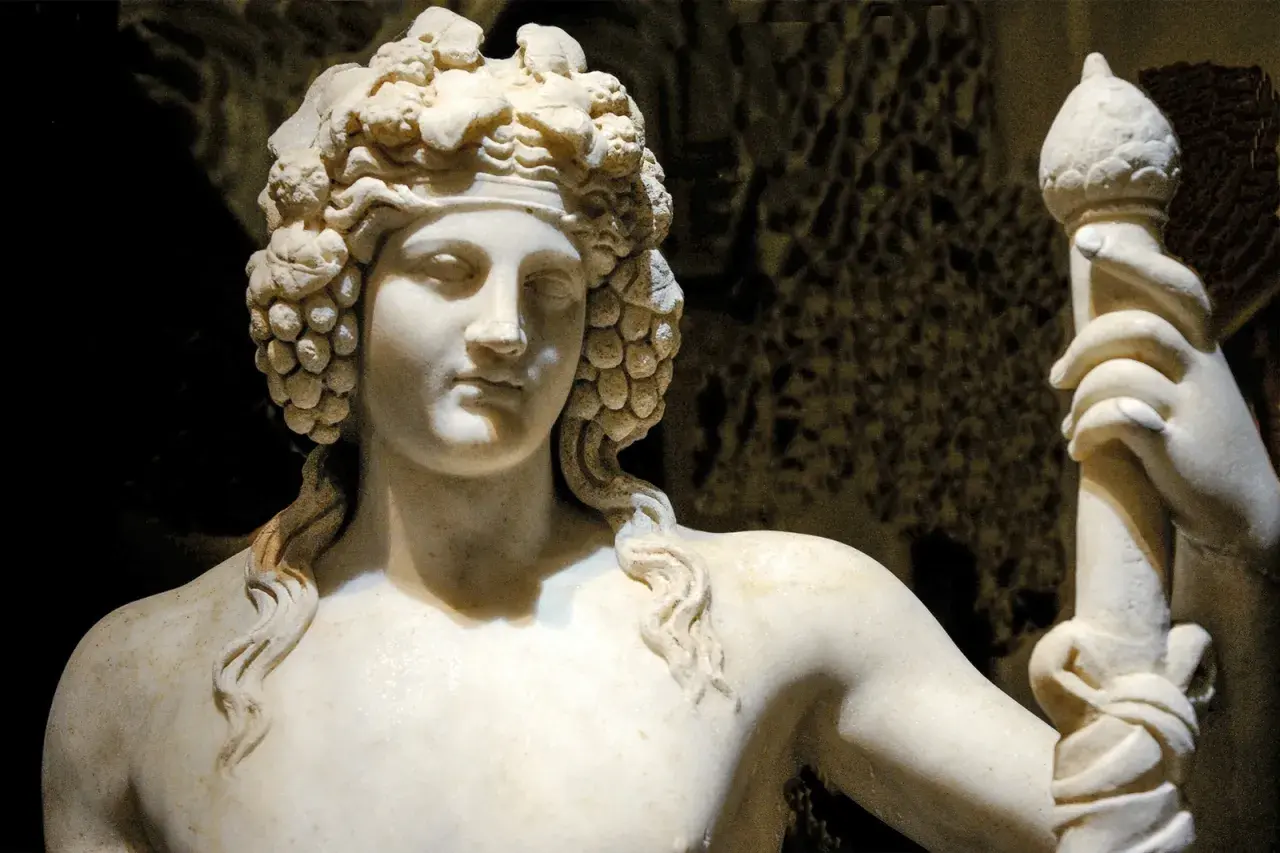 Sculpture de marbre d'une déesse du vin, couronnée de grappes de raisin, tenant un bâton orné.