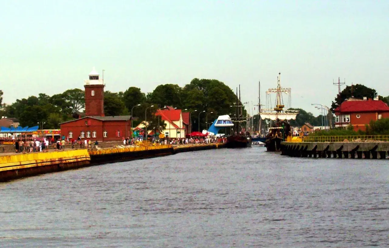 Widok na port z latarnią morską, statkami i ludźmi na nabrzeżu.