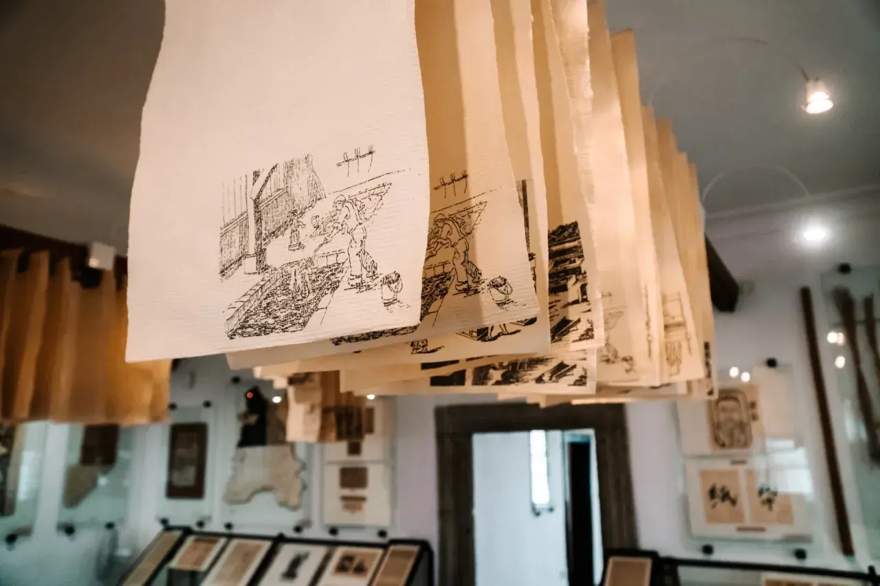 Rzędy ręcznie rysowanych scen na papierze czerpanym wiszą pod sufitem, tworząc unikalną galerię.