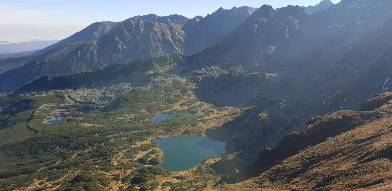 Widok na Tatry z licznymi stawami i kosodrzewiną. Szlak przez murowaniec prowadzi w kierunku górskich szczytów.