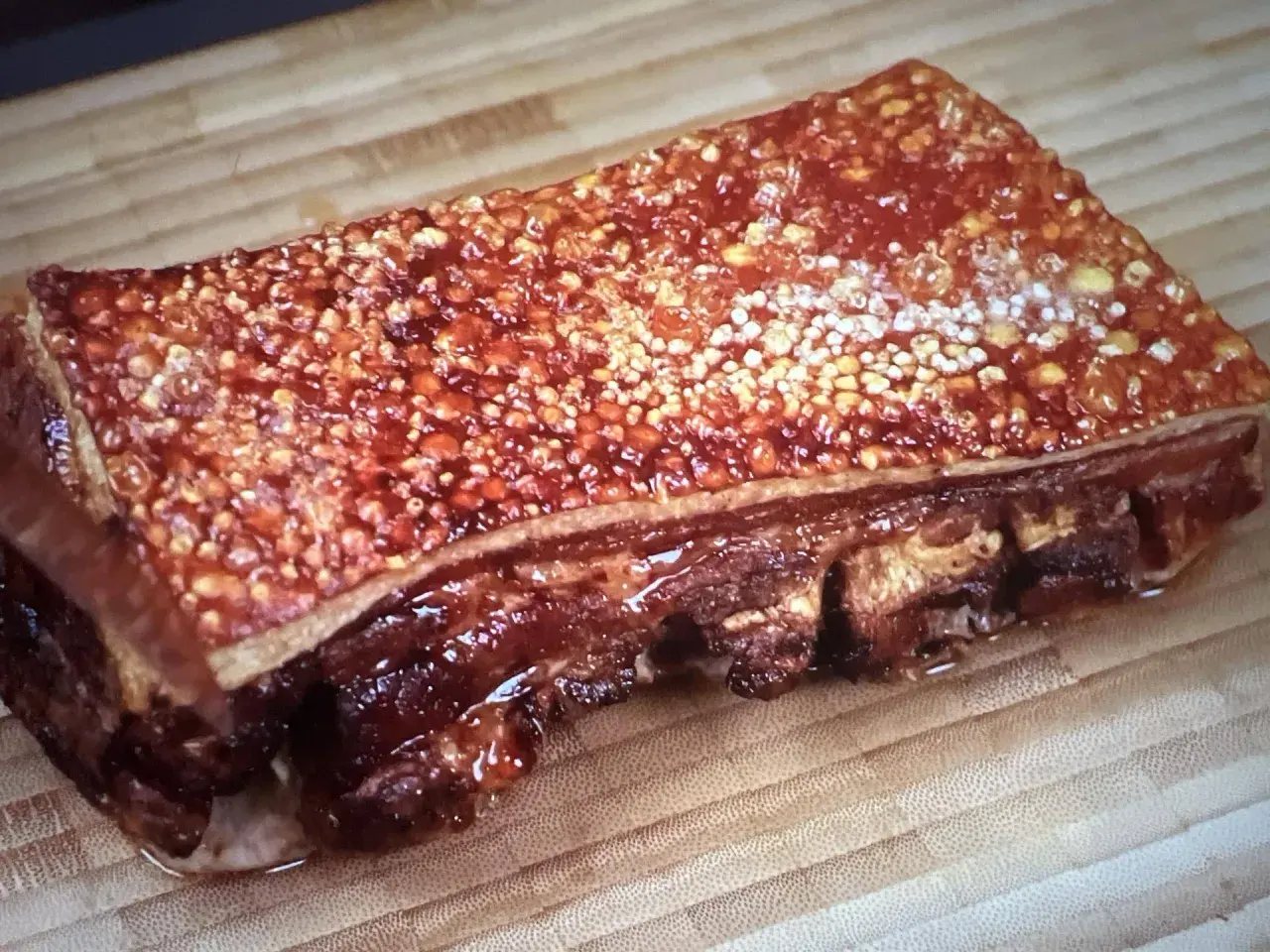 Poitrine de porc barbecue croustillante, avec une couenne dorée et des côtes apparentes, prête à être dégustée sur une planche en bois.