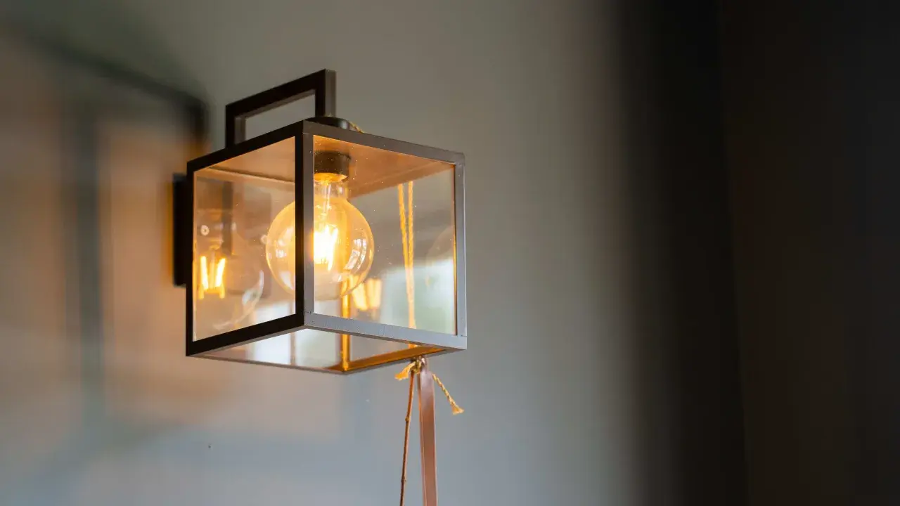 Aplique de foco con estructura metálica negra y cristal, iluminando con una bombilla de filamento.