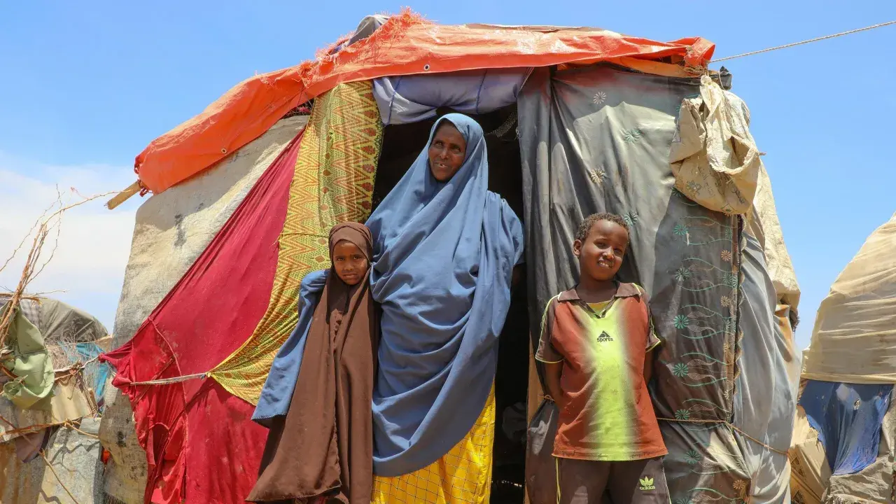 En kvinna och två barn står framför ett provisoriskt boende i Somalia. Deras historia är en del av Somalias historia.