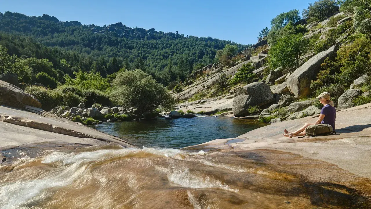 Una mujer descansa junto a unas pozas en Madrid, rodeada de naturaleza y rocas.