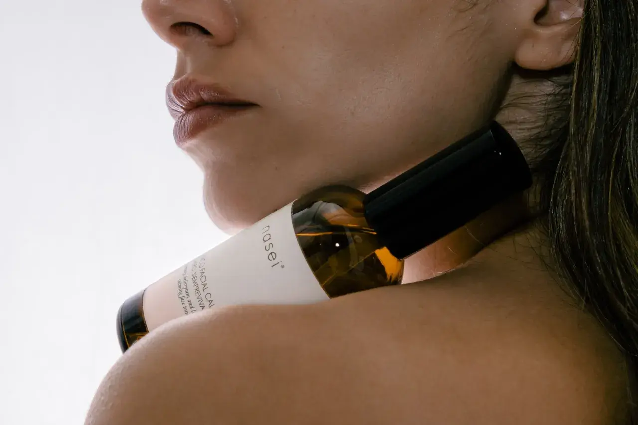 Labios y cuello de mujer con un frasco de sérum facial que contiene ácido hialurónico, para una piel radiante.