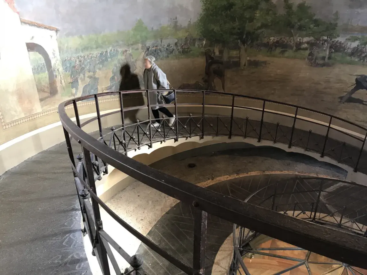 Una persona sale la scala a chiocciola all'interno della torre di San Martino, con un affresco di battaglia che decora le pareti.