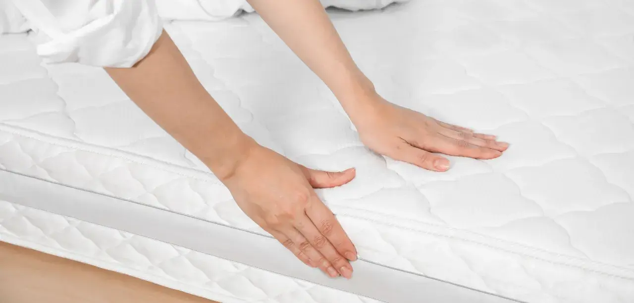 Mains palpant un matelas blanc, peut-être pour évaluer les symptômes d'un matelas trop ferme.