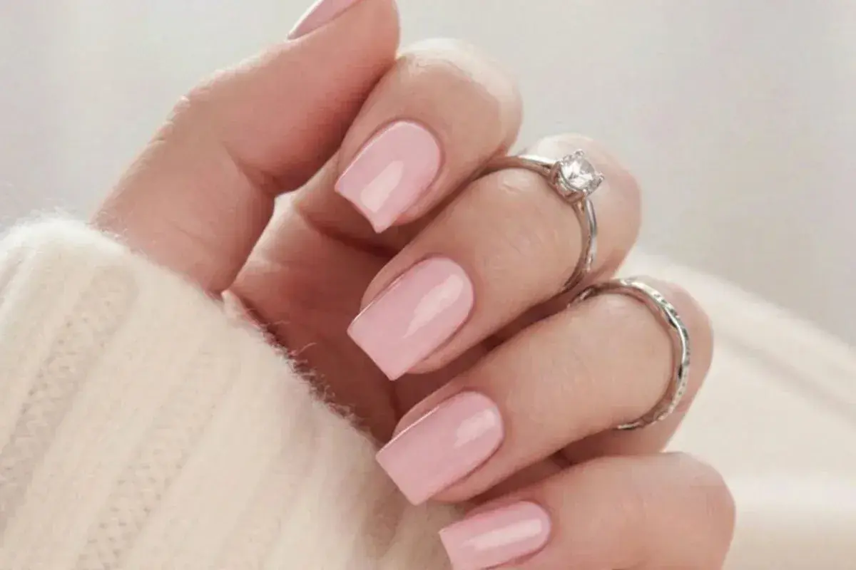 En hand med naglar målade i mjukt nagellack rosa, prydd med två silverringar.