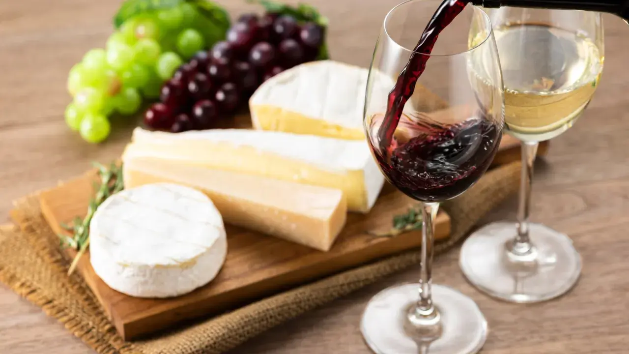Un bicchiere di vino rosso viene versato, accanto a formaggi assortiti e grappoli d'uva. L'abbinamento perfetto di vino per formaggi.