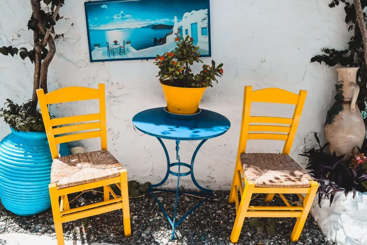 Zwei gelbe Stühle und ein blauer Tisch mit Blumentopf. Ein Bild mit Meerblick hängt an der Wand. Hier sind die Kos Geheimtipps für dein nächstes Foto!