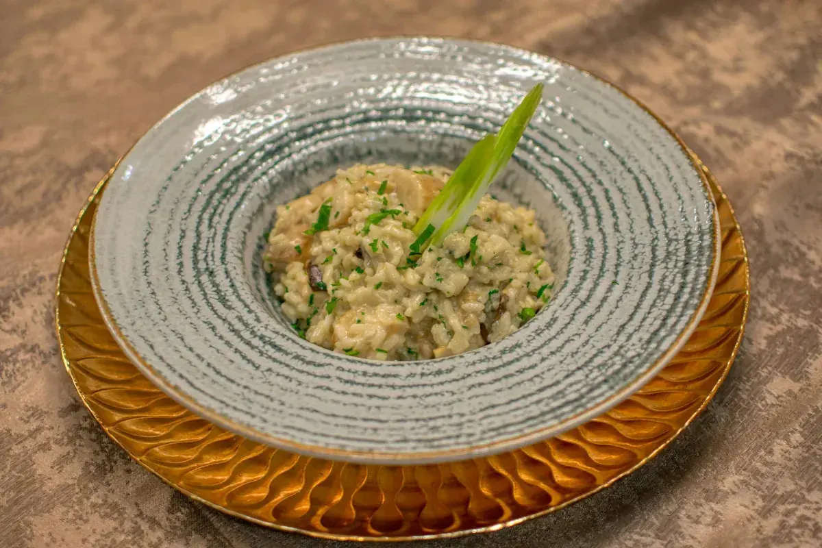 En krämig svamprisotto, kanske det godaste risotto receptet, serverad i en vacker skål med en grön garnityr.