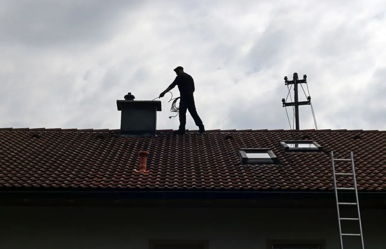 Kominiarz na dachu przygotowuje się do pracy. Zastanawiasz się, ile kosztuje szlamowanie komina?