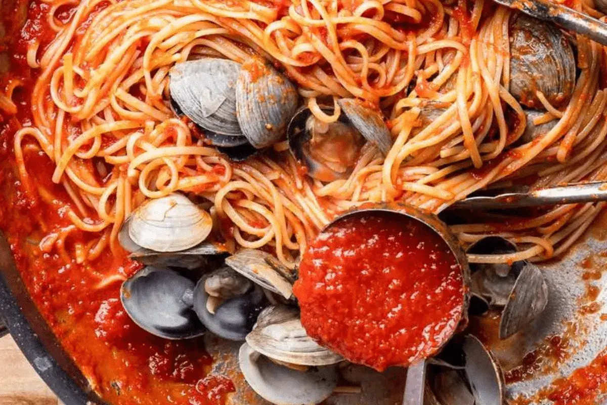 Spaghetti alle vongole, un plat de pâtes aux palourdes et sauce tomate, servi dans une poêle avec une louche de sauce.