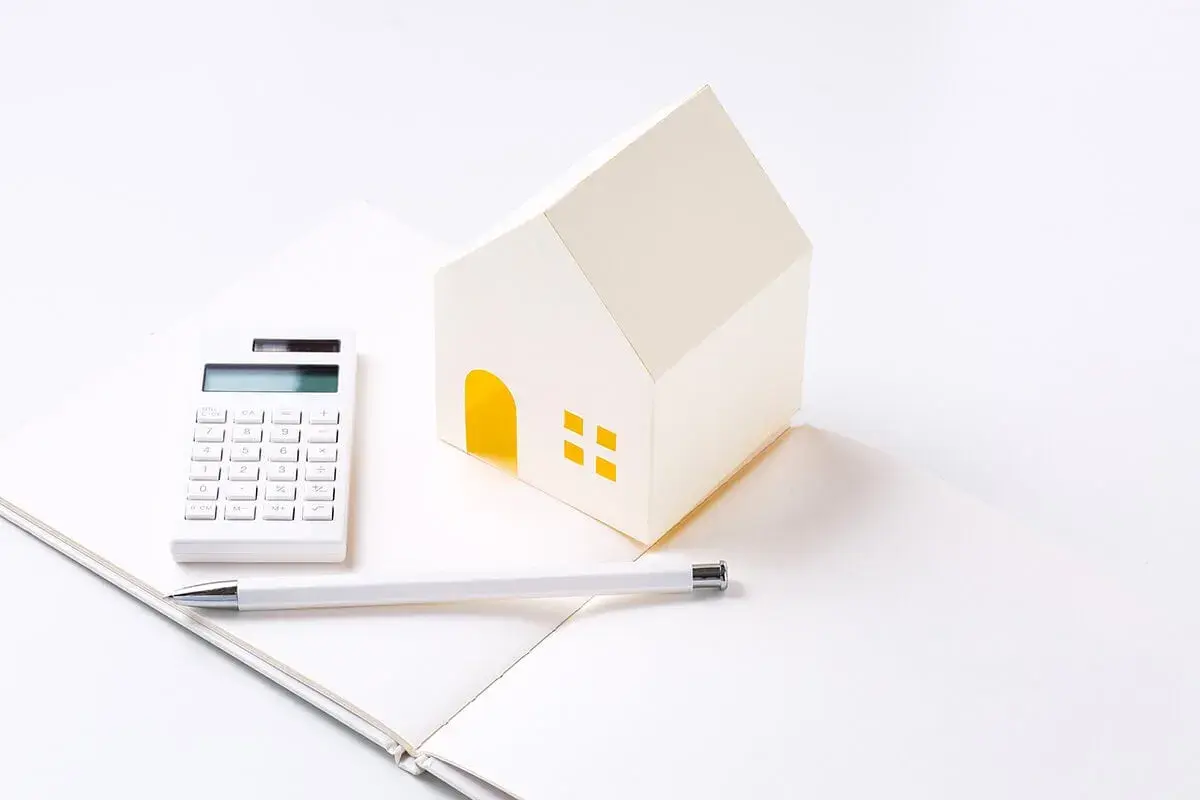 Maison en papier, calculatrice et stylo sur un carnet ouvert, symbolisant les **PTZ travaux soi-même**.