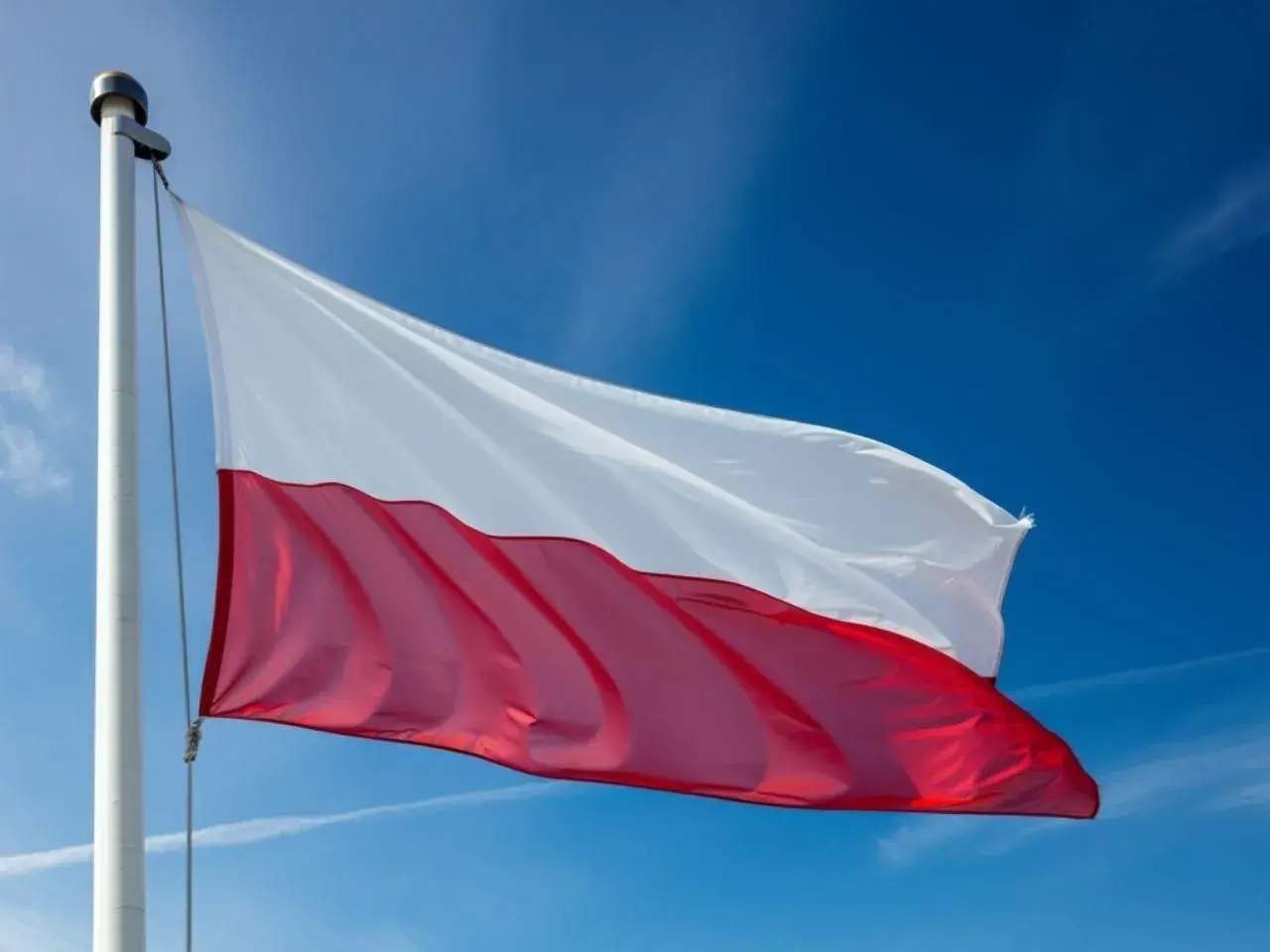Polska flaga powiewa na maszcie na tle błękitnego nieba.
