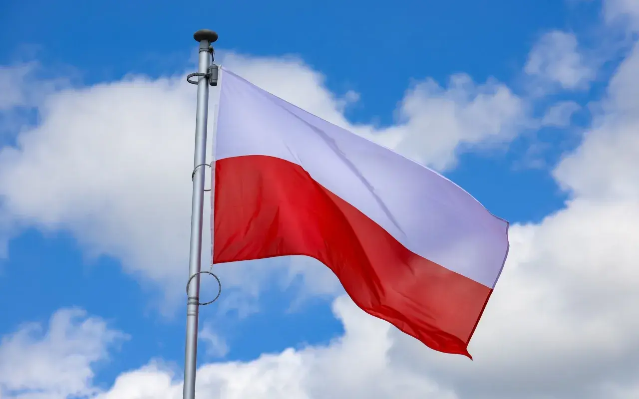 Biało-czerwona flaga Polski powiewa na tle błękitnego nieba z chmurami. Czy 2 maja jest wolny? To pytanie zadają sobie Polacy, ciesząc się świętem narodowym.