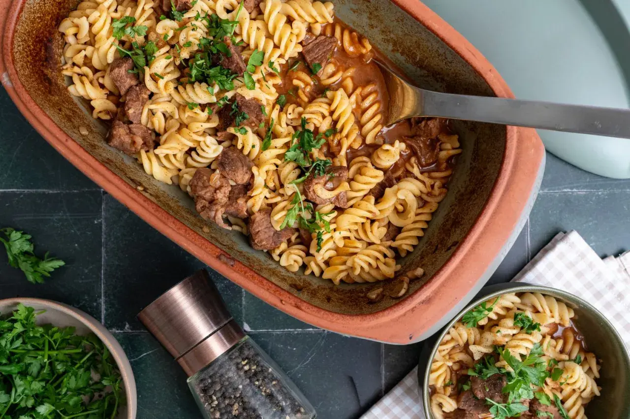 Herzhaftes Gulasch mit Nudeln, garniert mit frischer Petersilie, serviert in einem rustikalen Auflauf.