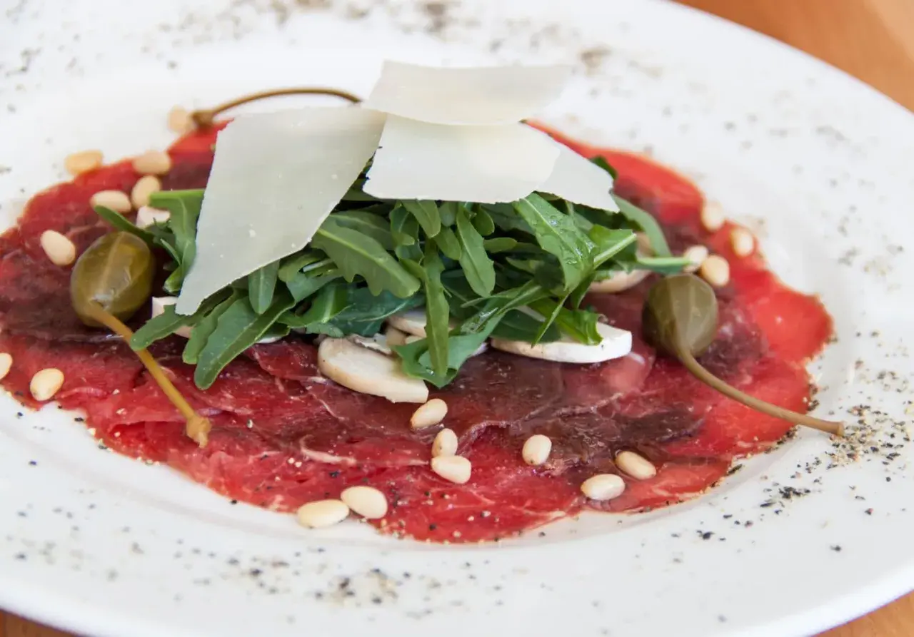 Delicato carpaccio di manzo con rucola, scaglie di parmigiano, pinoli, capperi e funghi champignon.