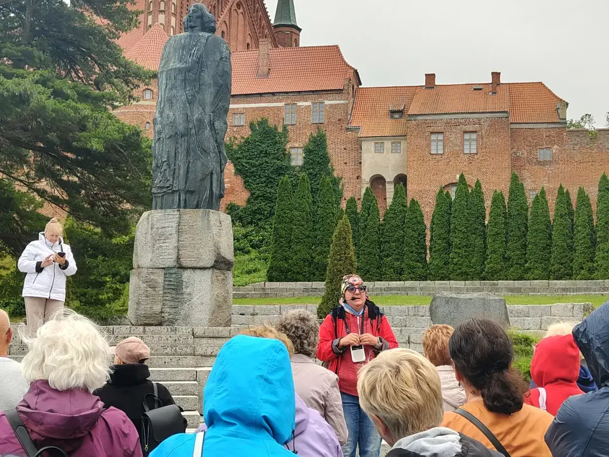 Wycieczka po Fromborku: przewodnik opowiada o Koperniku przy pomniku, w tle katedra. Atrakcje Fromborka odkrywane przez turystów.